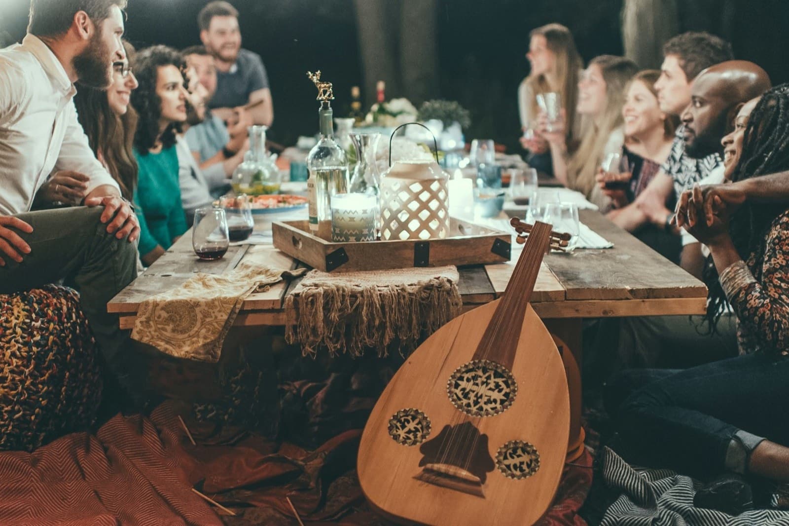 Gruppe von Freunden an einem langen Holztisch bei einem Gartenfest am Abend unter Lichterketten