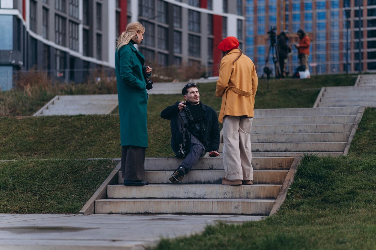 Drei junge Leute unterhalten sich auf einer Betontreppe im Freien vor modernen Wohngebäuden