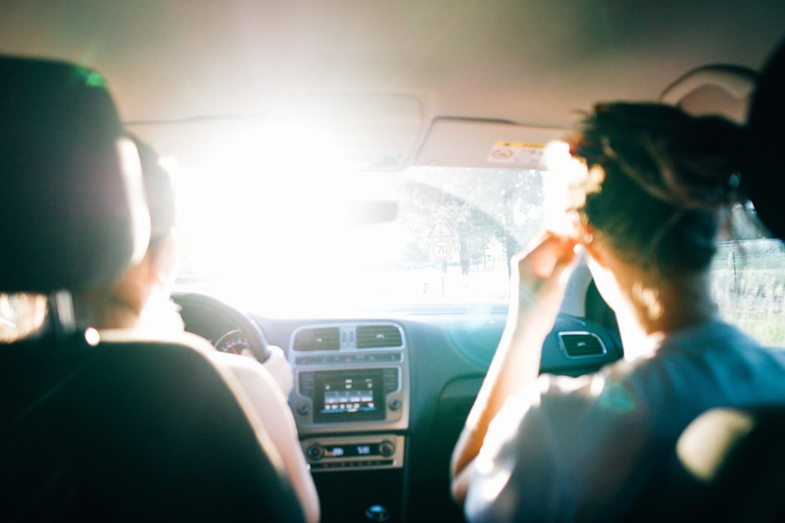 Blick vom Rücksitz eines Autos zwischen zwei Vordersitzen hindurch auf eine sonnige Landstraße