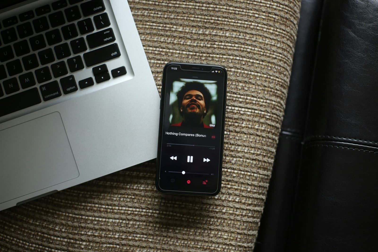 Smartphone mit laufender Musikapp neben einem aufgeklappten Laptop auf einem Sofa