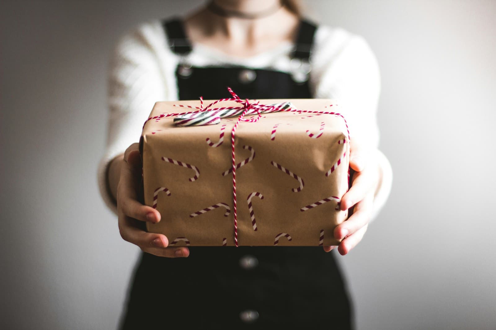Eine Person hält ein in Packpapier mit Zuckerstangenmuster eingewickeltes Geschenk mit rot weißer Kordel in die Kamera