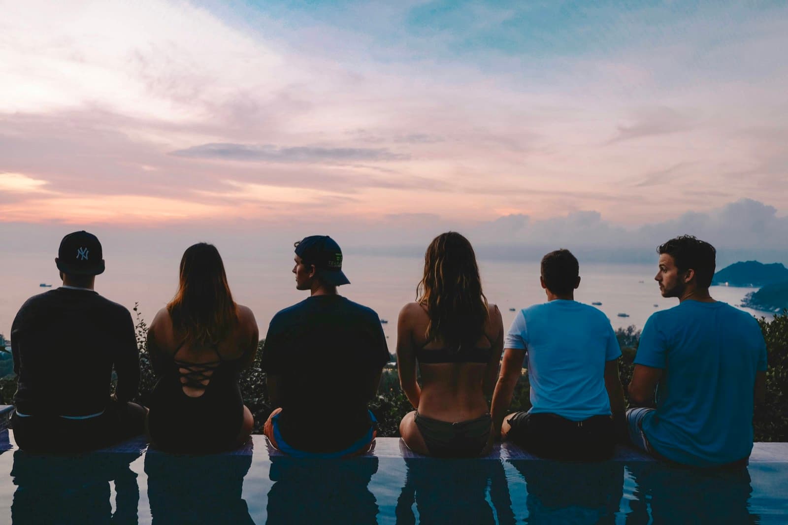 Sechs Personen sitzen am Rand eines Pools vor einem Ferienhaus