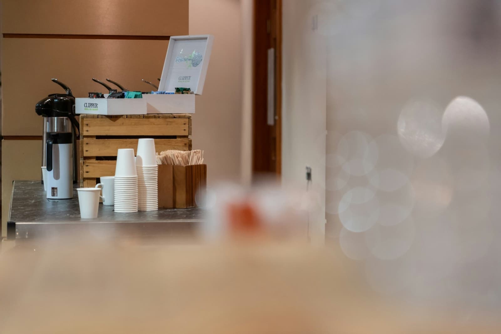 Kaffeestation im Büro mit Thermoskannen, Pappbechern, Rührstäbchen und einer Box mit Teebeuteln